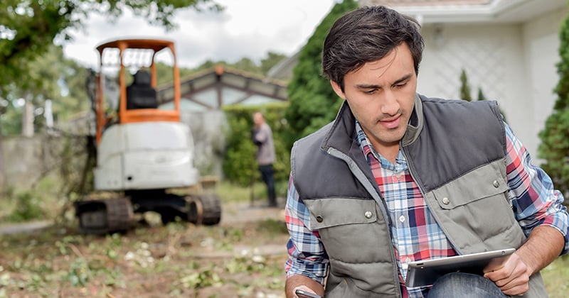Landscaper outside using tablet with digger in background